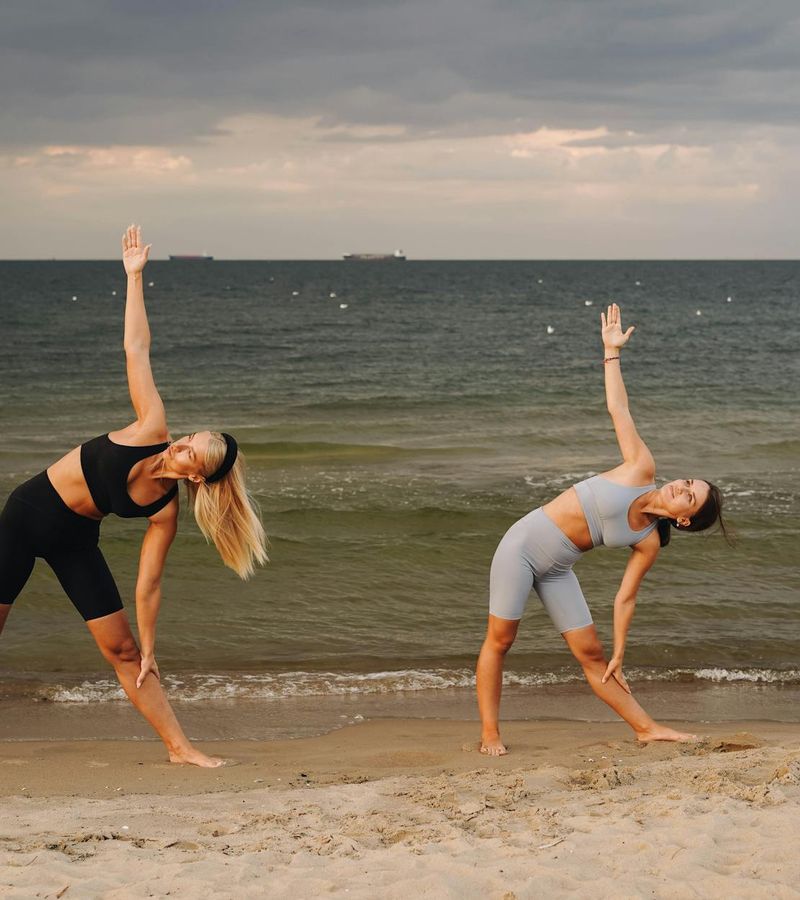 Person performing a warrior yoga pose on a beach during sunset.