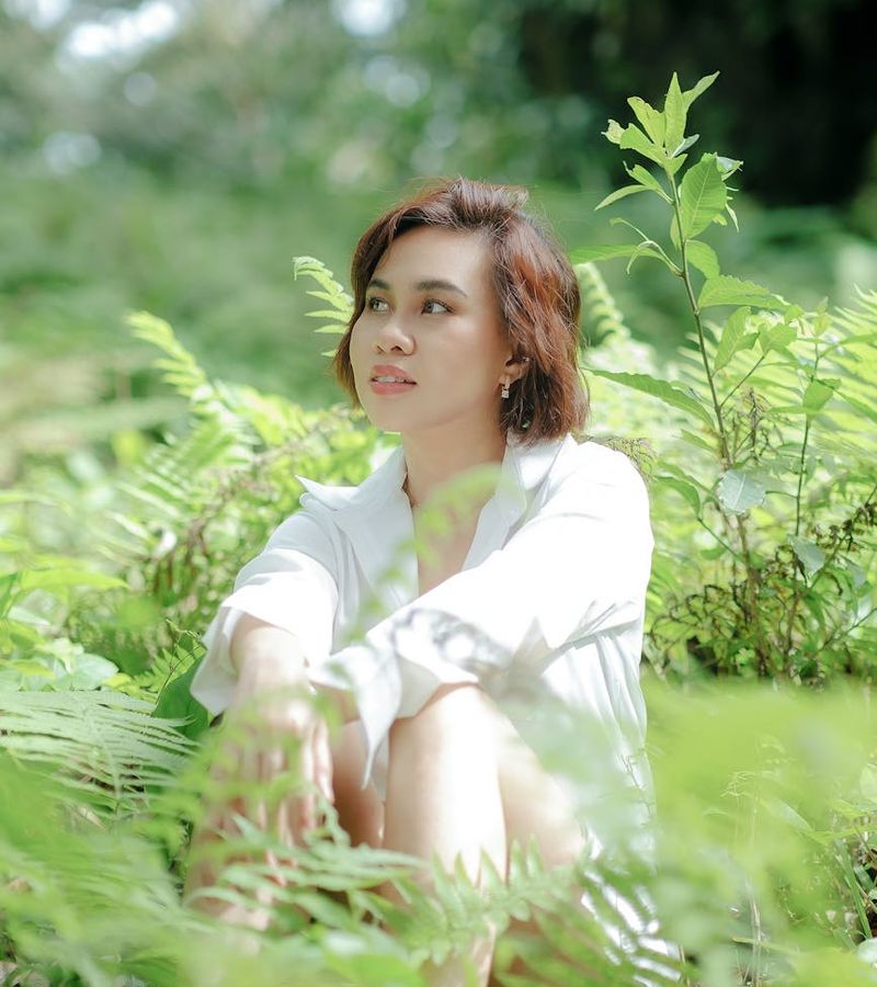 Woman meditating in a serene environment with green plants around.